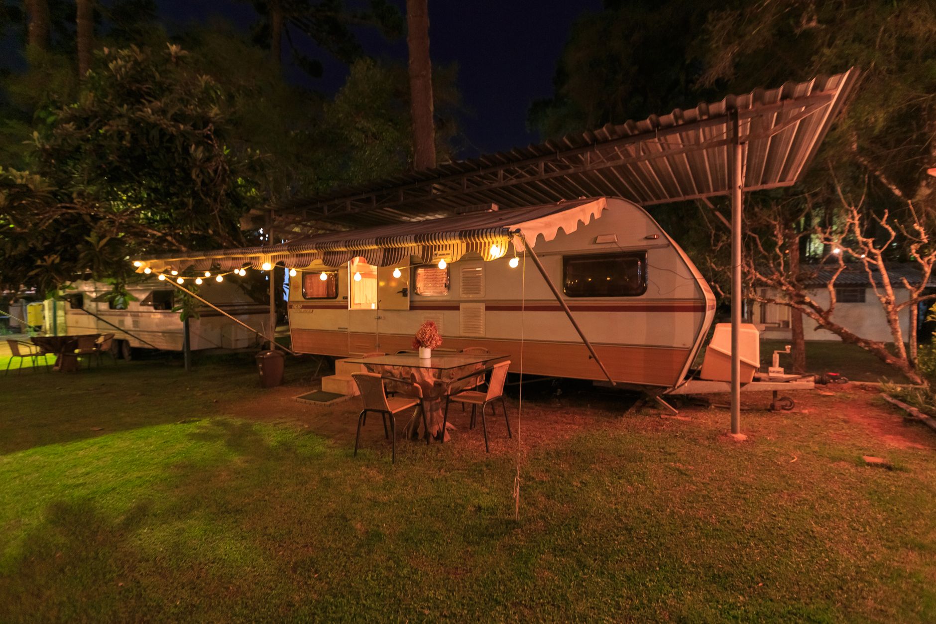 Charming retro camper trailer lit with warm lights, creating a cozy evening camping ambiance in nature.