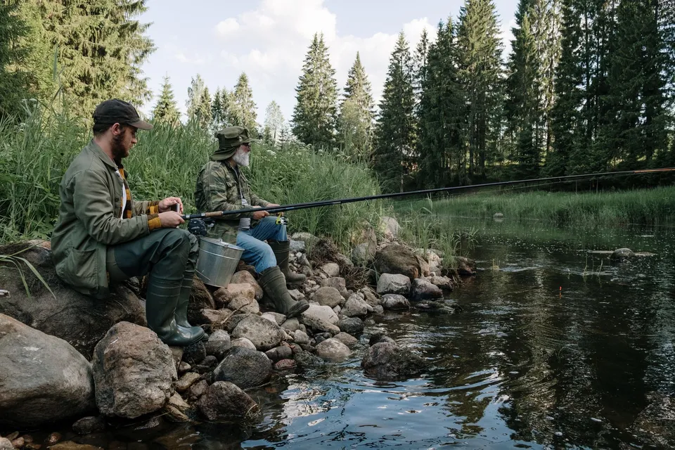 Two men enjoying a peaceful fishing trip by a forest riverbank, surrounded by nature.