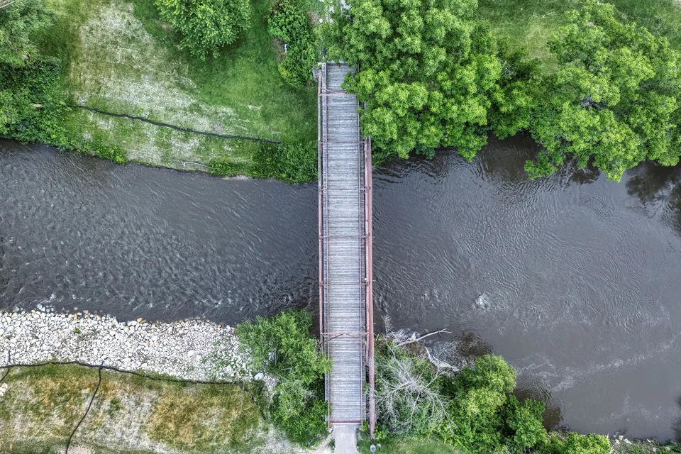 Aerial shot of a wooden bridge crossing a river surrounded by lush greenery in Lanesboro, Minnesota.